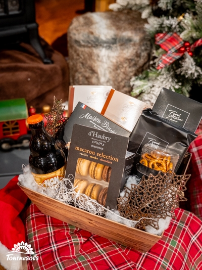 Panier garni Tournesols avec macaron, chocolats et bière devant un sapin.